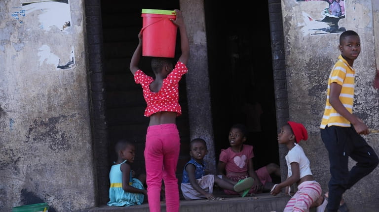 A young girl carries a bucket of water while entering...