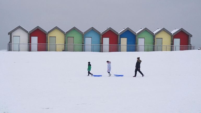 People walk through the snow beside the beach huts at...