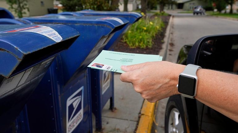 A person drops into a mail box applications for mail-in...