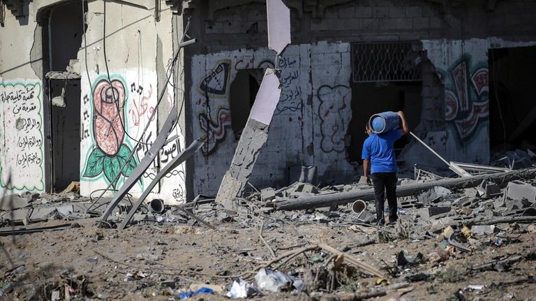 A Palestinian man carries a gas tank amid the rubble in Gaza...