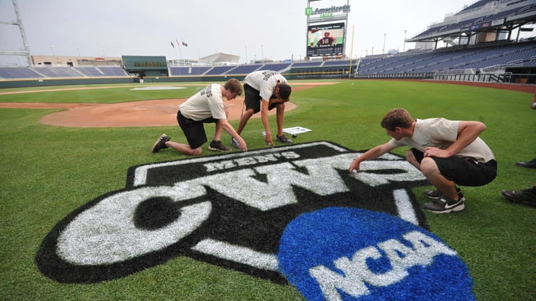 Grounds crew members paint the College World Series logo behind...