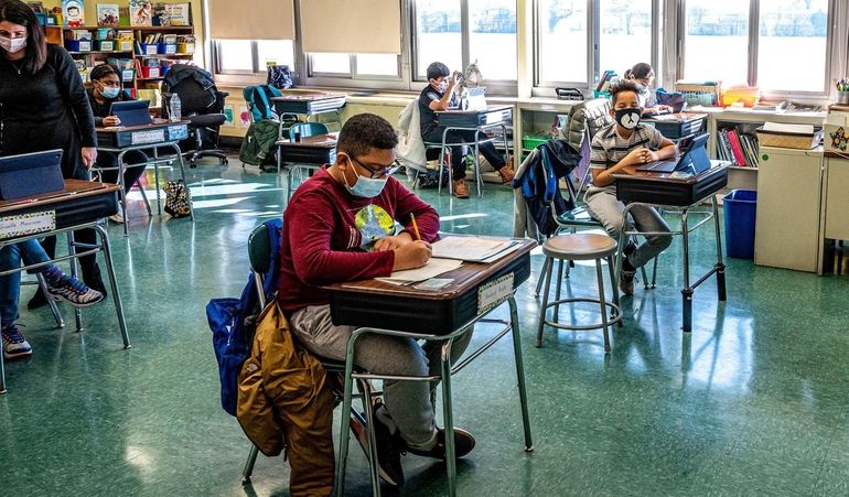 Elementary school students do their homework, with their masks on,...