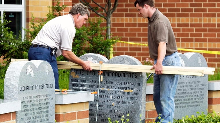 Workers remove a monument bearing the Ten Commandments outside West...