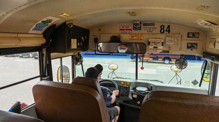 A school bus driver sits at the wheel of a...