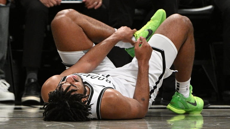 Nets guard Cam Thomas holds his left ankle after injuring...