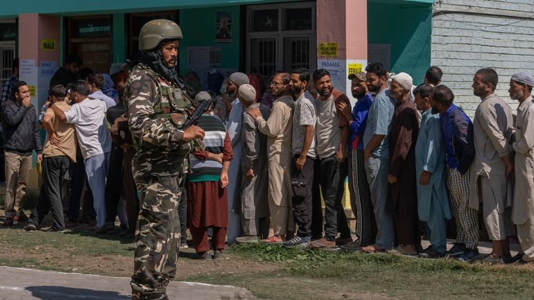 An Indian paramilitary soldier stands guard as people queue up...