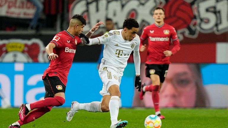 Bayern's Jamal Musiala, center, and Leverkusen's Piero Hincapie, left, challenge...