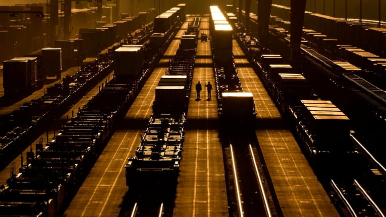 Workers walk among shipping containers in a loading area at...