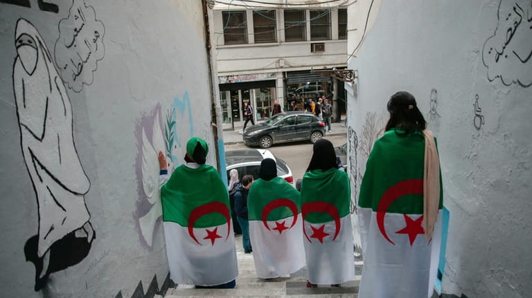Young Algerian women pose next to street art supporting the...