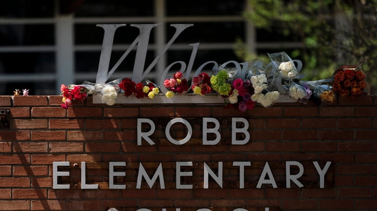Flowers are placed around a welcome sign outside Robb Elementary...