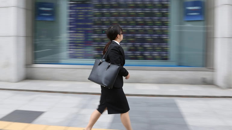A woman walks by an electronic stock board of a...