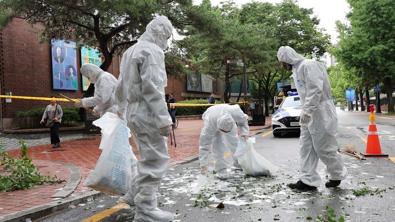 Officers wearing protective gear collect the trash from a balloon...