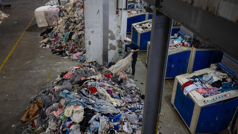 A worker feeds discarded textiles to a shredding machine at...