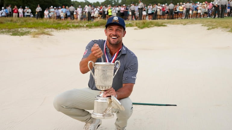 Bryson DeChambeau holds the trophy in the bunker after winning...