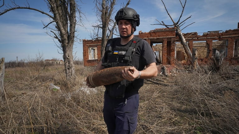A Ukrainian Emergency Situation sapper carries an unexploded shell after...