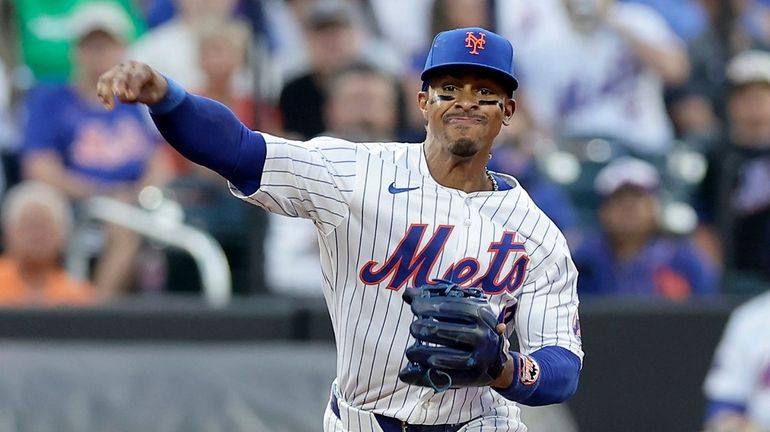 Francisco Lindor of the Mets throws to first base to...