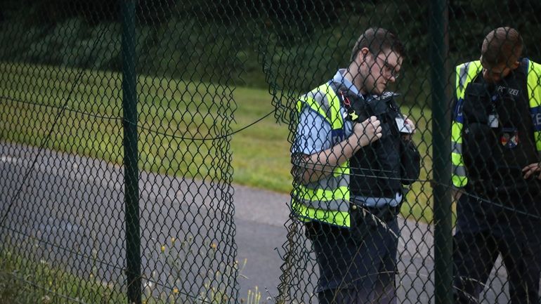 Police officers stand next to a hole in the fence...