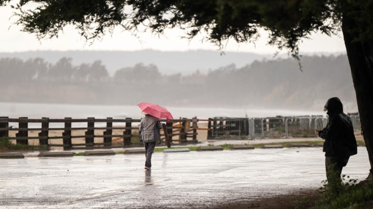 People walk through wet conditions along Seacliff State Beach in...