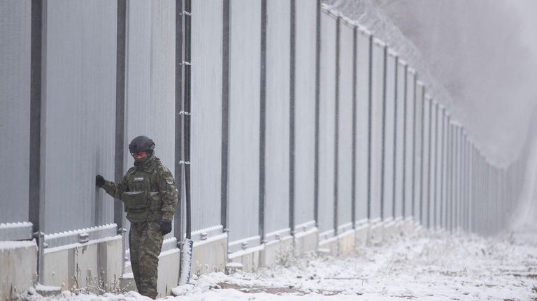 Polish border guard stands next to the border wall in...