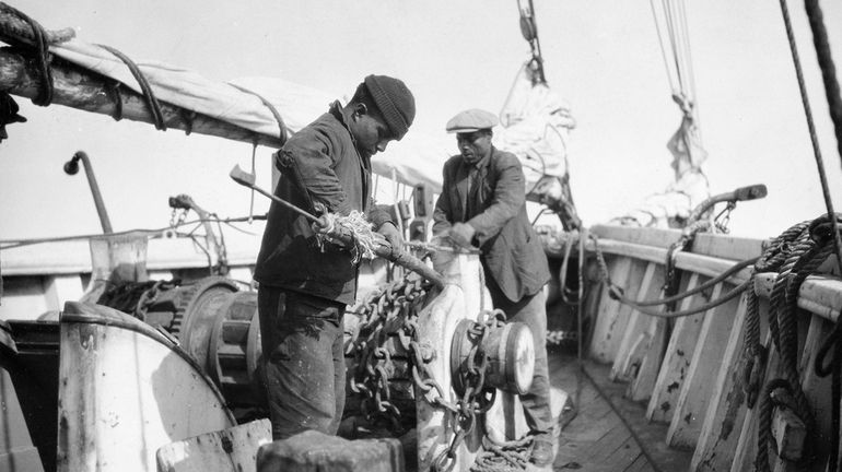 Sailors fasten a harpoon to a pole aboard a whaling ship...