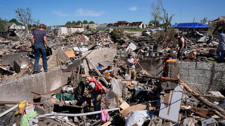 Family members clean belongings out of a tornado damaged home,...