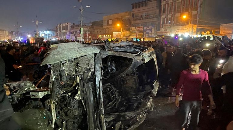 Iraqis gather at the site of a burned vehicle targeted...