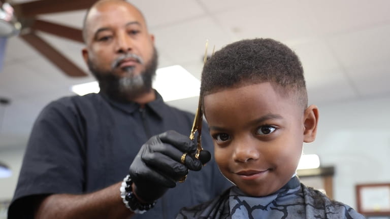 Matthew Fullington, 5, receives a haircut from Barber Ralston Holung,...