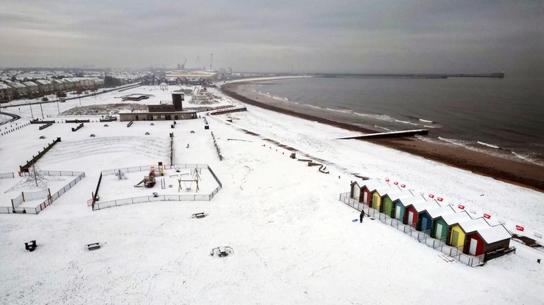 People walk through the snow beside the beach huts at...