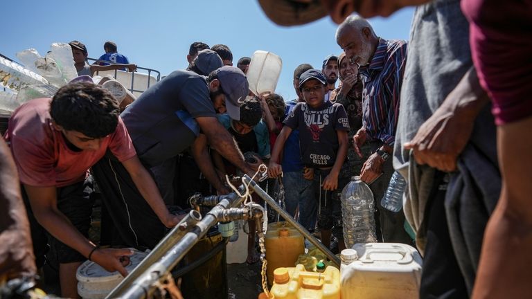 Displaced Palestinians line up to collect water, in Deir al...