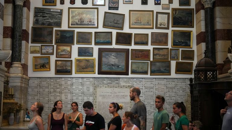 Visitors stand near paintings of ships in the Notre Dame...