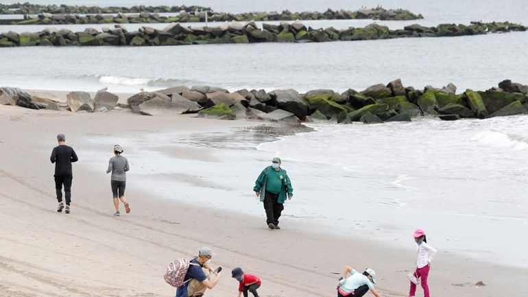 FILE- Children play in the sand while others jog as...