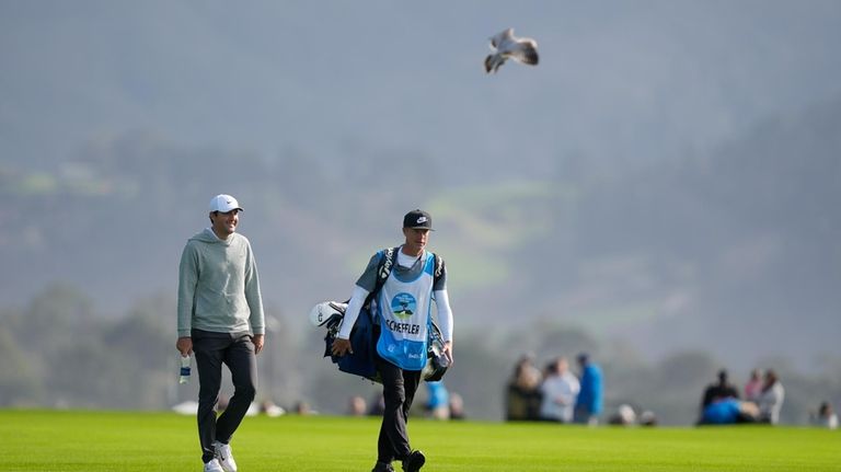 Scottie Scheffler, left, walks with his caddie up the 14th...