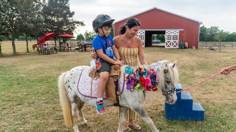 Maria Ioannou helps her son Raphael, 6, from Southold ride...