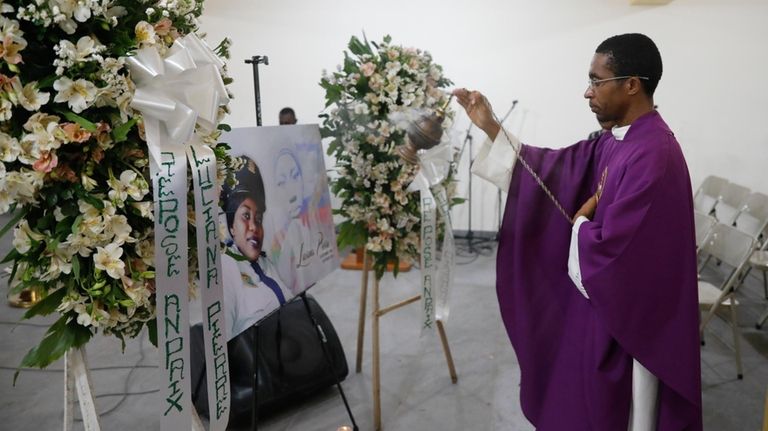 A priest swings incense in front of a photo of...