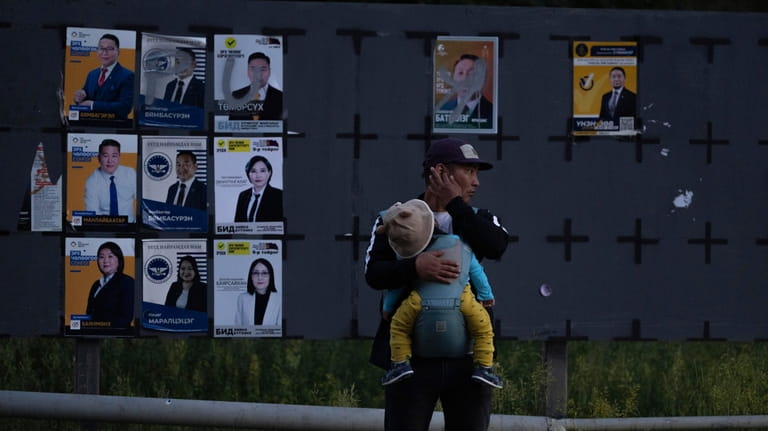 A man carries a child near candidates' posters two days...