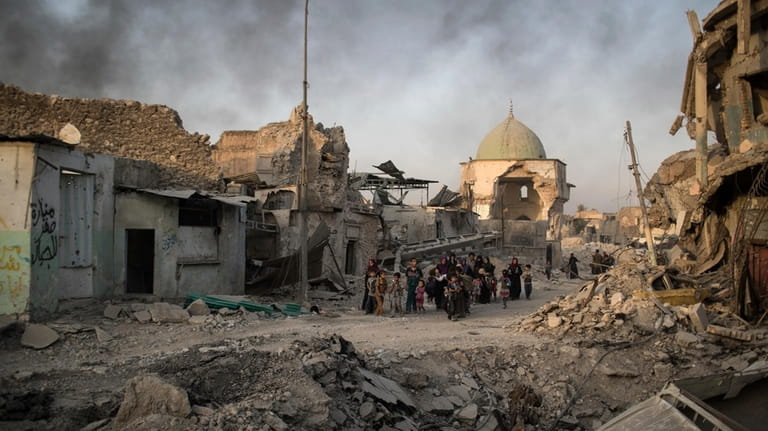 File - Fleeing Iraqi civilians walk past the heavily damaged...