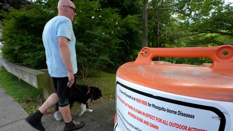 A passer-by walks a dog, Monday, Aug. 26, 2024, while...