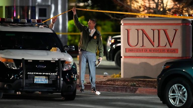 A police officer walks under crime scene tape in the...