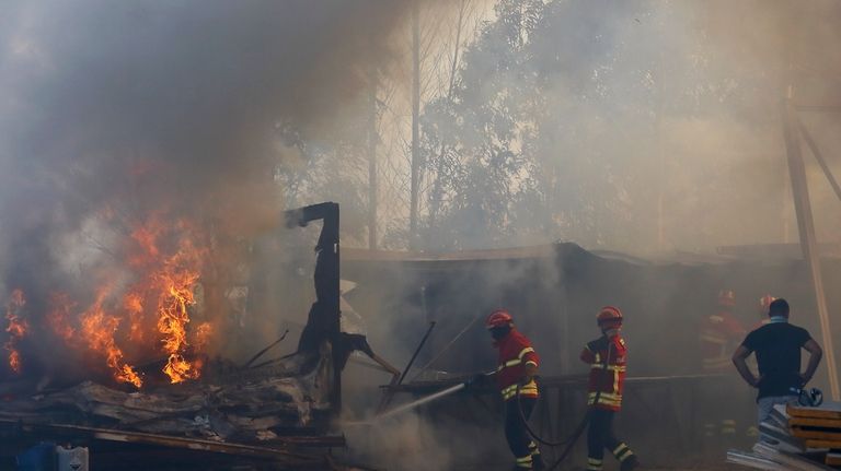 Firefighters work to control a fire next to warehouses in...