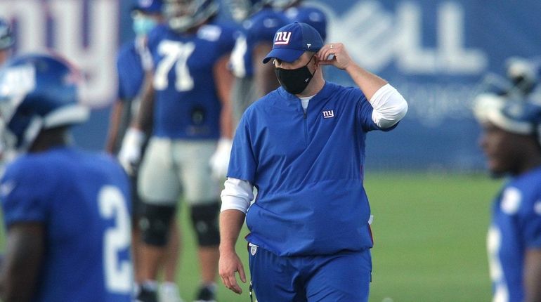 Giants head coach Joe Judge adjusts his mask as he...