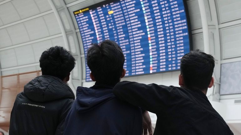 Passengers look up at the departure board as they wait...