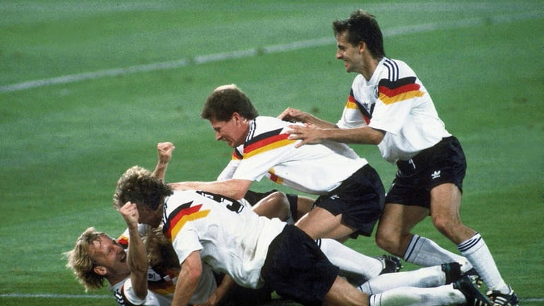 Germany players celebrate after Andreas Brehme, left on ground, scores...