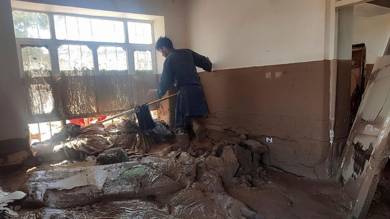 An Afghan man collects his belongings from his damaged home...