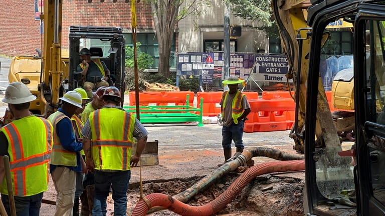 Workers try to fix a leaking water main junction on...
