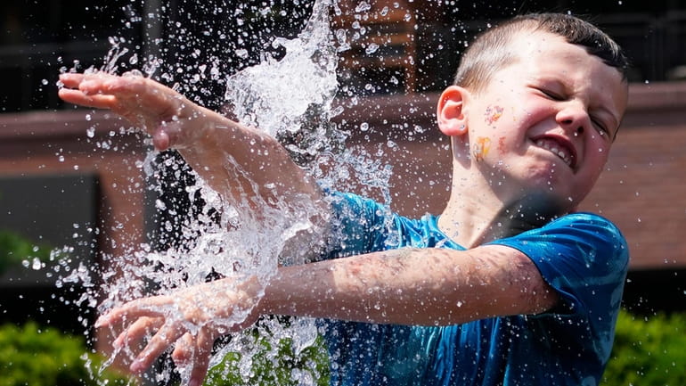 A boy cools off at a fountain during hot weather...