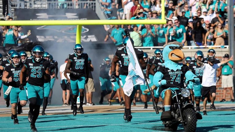 Mascot Chauncey the Chanticleer, front right, leads Coastal Carolina players...