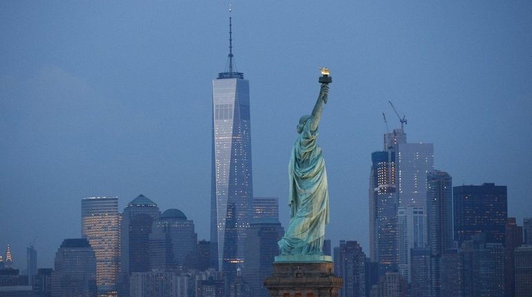 The Statue of Liberty stands in the foreground as Lower...