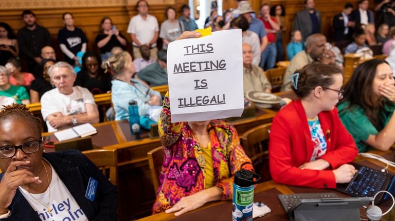 An attendee holds a sign that says "This Meeting is...