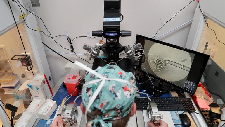 Lab staff use a microscope stand and articulated hand controls...