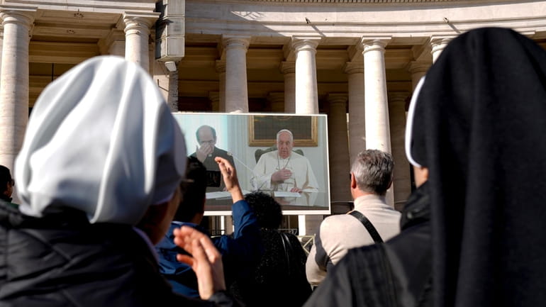 Nuns look at Pope Francis on a giant monitor set...